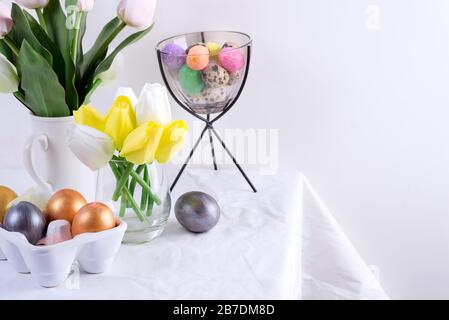 Congratulation Easter card of served table with spring flowers and handmade painted eggs against light grey wall. Stock Photo