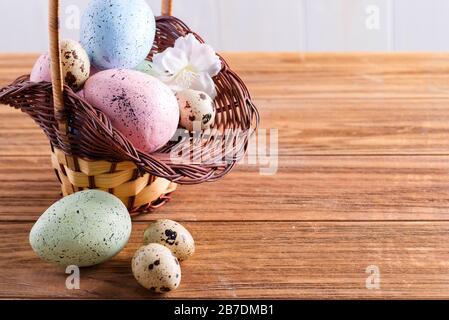 Festive Easter wicker basket with handmade painted chicken and quail eggs on a wooden table. Stock Photo