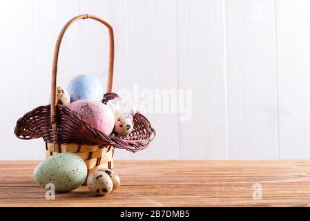 Festive Easter wicker basket with handmade painted chicken and quail eggs on a wooden table. Stock Photo