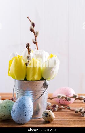 Happy Easter card with fresh spring tulips flowers in a bucket and handmade painted eggs on a wooden table. Stock Photo