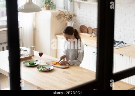 Smiling young woman cutting vegetables, cooking salad in kitchen Stock Photo