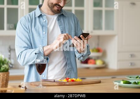 Smiling man using smartphone, cooking salad, preparing vegetables Stock Photo