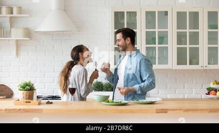 Happy loving couple singing, having fun with kitchenware in kitchen Stock Photo