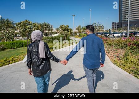 Muslim couple in love walking outdoors in a park while holding hands Stock Photo