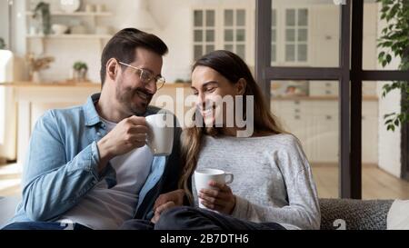 Happy loving couple relaxing on couch, drinking hot beverages Stock Photo