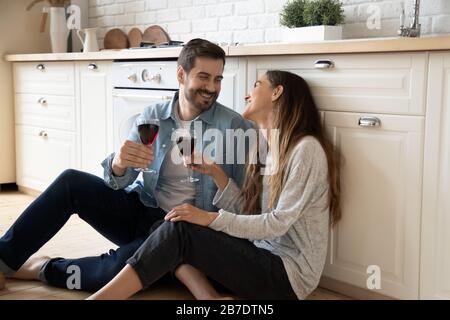 Happy young wife and husband drinking wine, sitting on floor Stock Photo