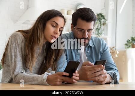 Young couple using smartphones, discussing news, looking at screen Stock Photo