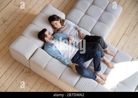 Loving couple holding hands, relaxing on cozy sofa top view