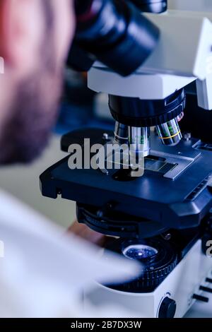 Scientific handling a light microscope examines a laboratory sample for ...