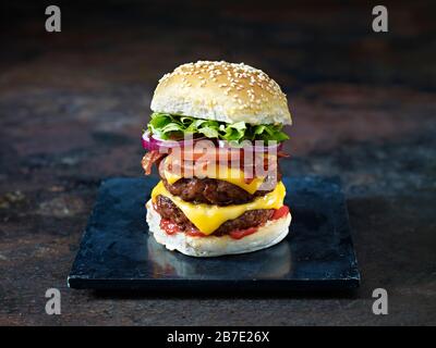 A bacon and double cheese burger against a dark background Stock Photo