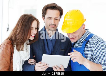 Worker and couple using tablet pc at construction site planning renovation house design plans Stock Photo