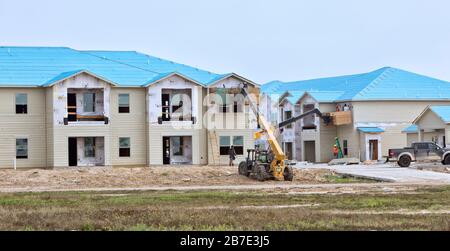 Rebuilding Salt Grass Landing Apartments. Workers installing window trim,  elevated with Caterpillar material lifter. Stock Photo