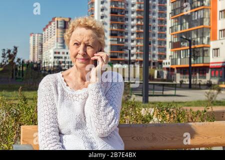 Relaxed elder woman sitting on a bench looking at camera and smiling Stock Photo