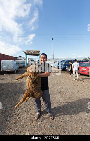 Kyrgyz man carrying sheep in the live stock market, in Tokmok, Kyrgyzstan Stock Photo