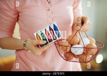 Closeup on female holding basket with eggs and food coloring in the living room in sunny spring day. Stock Photo