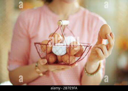 Closeup on female holding basket with eggs and showing egg in the living room in sunny spring day. Stock Photo