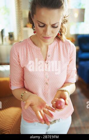 unhappy elegant female in a pink blouse and easter bunny ears looking at hands stained with a red easter egg in the modern living room in sunny spring Stock Photo