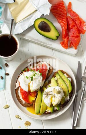 Morning breakfast. Poached egg boiled sandwich with avocado, salmon and coffee on a wooden table. Top view flat lay background. Stock Photo