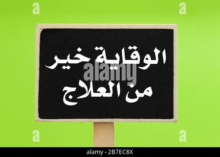 Prevention Is Better Than Cure written in Arabic (الوقاية خير من العلاج ) on a chalkboard against green background Stock Photo