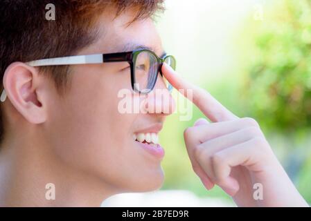 Closeup face Asian handsome teenage boy wearing glasses, Portrait cheerful hipster young man smile with a happy at park on green nature background in Stock Photo