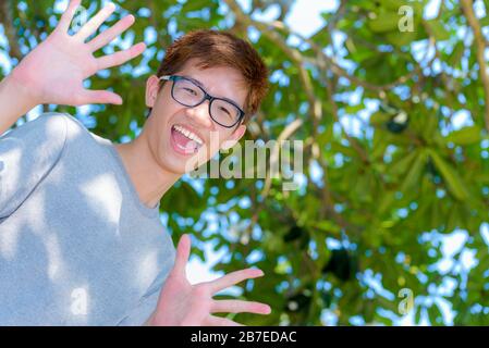 Low angle shot handsome Asian teenage boy wearing glasses fun, Portrait cheerful hipster young man are looking and laugh with a happy face at park on Stock Photo