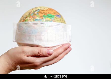 Medical mask on globe in female hand, coronavirus pandemic in world. Concept of global quarantine during the COVID-19 Stock Photo