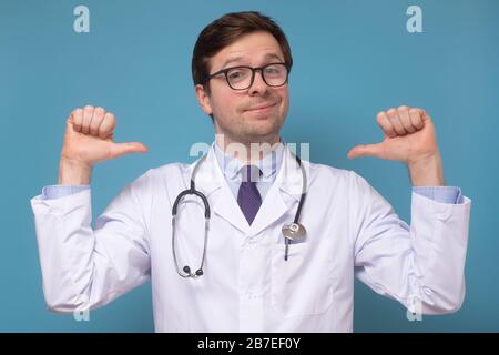 Caucasian young medical man intern or doctor feeling proud and self assured triumphing, being winner pointing at himself with thumbs tilting chest. St Stock Photo