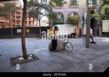Glovo delivery rider sits on a bollard beside his bike waiting for an order in central Madrid during the COVID-19 state of emergency Stock Photo