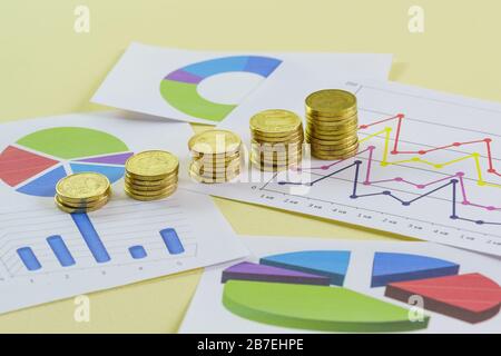 Increasing in size stacks of gold coins and colored graphics on a yellow background. Preparation of the report to investors on the financial condition