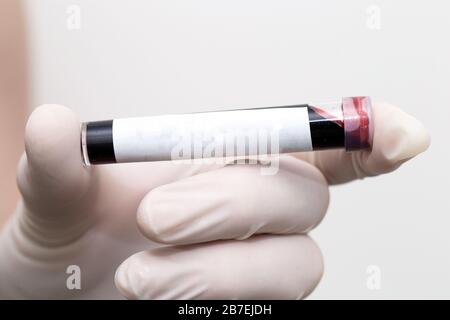 Hand with medical glove of scientist or doctor holds test tube with blood sample and blank label for own text Stock Photo