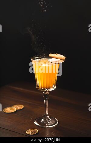 A glass of white mulled wine with a pear sprinkled with icing sugar on a dark background. Hot alcoholic drink in moody style. Stock Photo