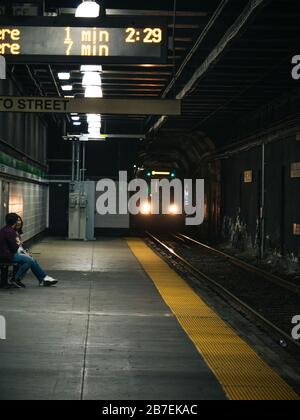 Man and a woman sitting and talking on a bench in a subway with upcoming train Stock Photo