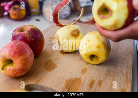 Closeup of wooden cutting board and person hands peeling old red apples fruit after harvest for cooking ingredient Stock Photo