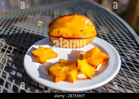 Closeup of sliced orange yellow starfruit on plate on metal table outside with vibrant color Stock Photo