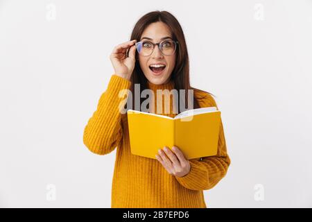 Image of beautiful brunette adult woman wearing eyeglasses making notes in diary book isolated over white background Stock Photo