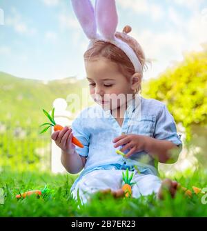 Portrait of a cute little baby boy dressed as an Easter bunny, adorable kid playing with carrots and wearing big furry rabbit ears, happy child Stock Photo
