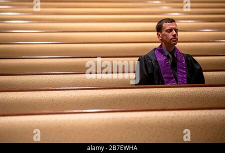 Mar 15, 2020; Springfield, IL, USA; Associate pastor Justin Snider prays from the pews as Rev. Roger Grimmett delivers his message as First United Methodist Church takes their Sunday morning service live online for the first time due to restrictions of large gatherings because of COVID-19, Sunday, March 15, 2020, in Springfield, Ill. First United Methodist Church live streamed their 9 a.m. traditional service as well as their 10:30 a.m. contemporary service on the church's Facebook page because of the restrictions. It's the first time the church has closed to corporate worship since 1918 at th Stock Photo