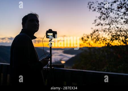 Fog mist clouds on mountains with man doing timelapse in morning at new river gorge valley in Grandview Overlook, West Virginia during morning sunrise Stock Photo