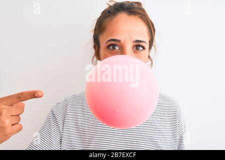 Young redhead woman chewing gum and blowing hair bubble over white isolated background very happy pointing with hand and finger Stock Photo