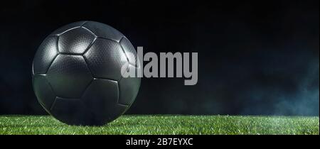 Low-angle close-up of a black soccer ball on the green grass of the football ground against dark background for copy space Stock Photo