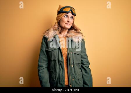 Middle age beautiful blonde skier woman wearing snow sportwear and ski goggles smiling looking to the side and staring away thinking. Stock Photo