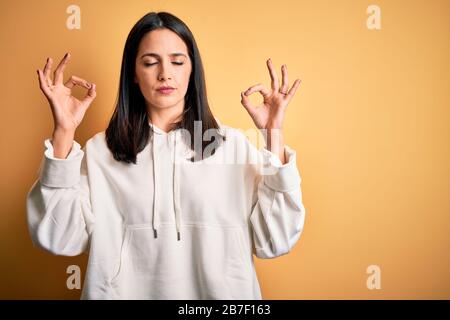 Young brunette sportswoman with blue eyes wearing training sweatshirt over yellow background relax and smiling with eyes closed doing meditation gestu Stock Photo