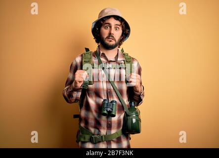 Young hiker man with curly hair and beard hiking wearing backpack and water canteen In shock face, looking skeptical and sarcastic, surprised with ope Stock Photo