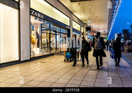 Warsaw, Poland - December 19, 2019: Spanish Zara fast fashion store sign entrance with people walking on Marszalkowska street sidewalk at night with C Stock Photo