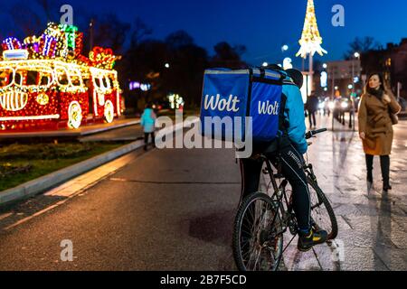Warsaw, Poland - December 20, 2019: Wolt courier in blue work clothes delivery man delivering online food orders on bicycle in winter at night evening Stock Photo
