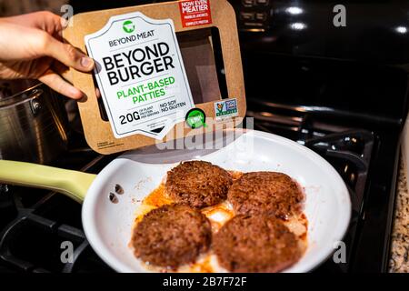 Herndon, USA - February 3, 2020: Man male hand holding Beyond Burger package of plant-based patties with burgers cooking on frying pan on top of stove Stock Photo