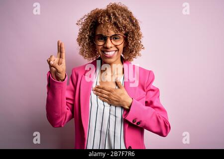 Young african american businesswoman wearing glasses standing over pink background smiling swearing with hand on chest and fingers up, making a loyalt Stock Photo