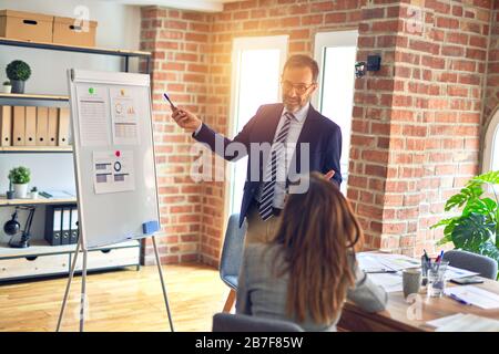 Two middle age business workers smiling happy and confidentt working together with smile on face. Man standing doing work presentation using board and Stock Photo