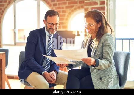 Two middle age business workers smiling happy and confident. Working together with smile on face reading documents at the office Stock Photo