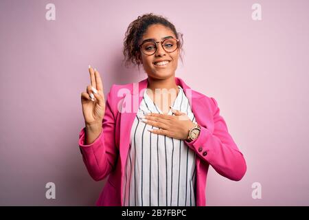 Beautiful african american businesswoman wearing jacket and glasses over pink background smiling swearing with hand on chest and fingers up, making a Stock Photo